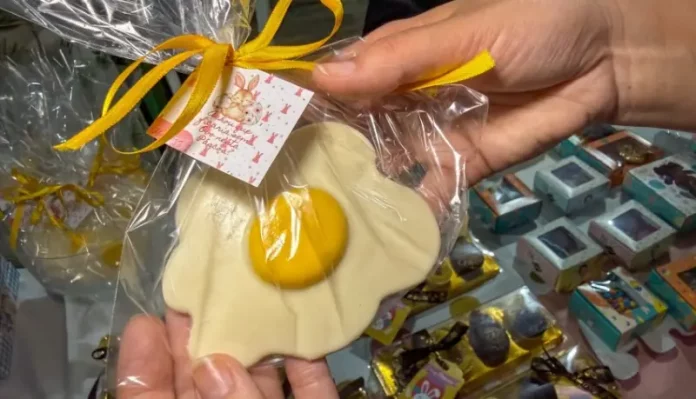 Pessoa segura um doce artesanal em formato de ovo frito, embalado para presente, representando produtos criativos de pequenos negócios para a Páscoa.