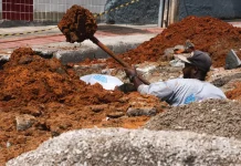 Trabalhador realiza escavação em via urbana para implantação do Plano Diretor de Drenagem Urbana em São José, ilustrando ações de infraestrutura para prevenção de alagamentos e melhoria do escoamento da água.