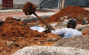 Trabalhador realiza escavação em via urbana para implantação do Plano Diretor de Drenagem Urbana em São José, ilustrando ações de infraestrutura para prevenção de alagamentos e melhoria do escoamento da água.