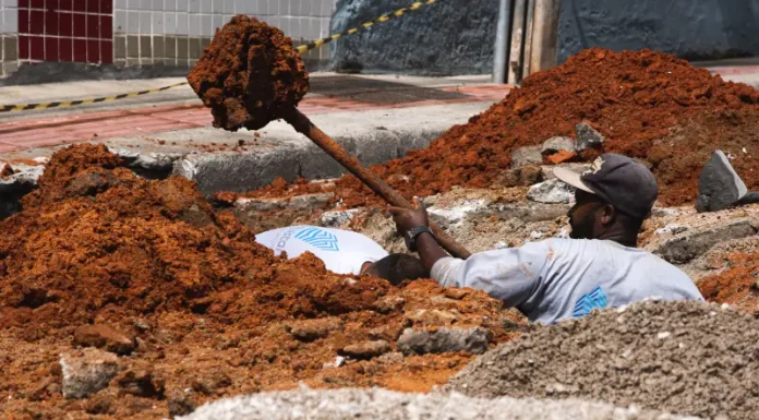 Trabalhador realiza escavação em via urbana para implantação do Plano Diretor de Drenagem Urbana em São José, ilustrando ações de infraestrutura para prevenção de alagamentos e melhoria do escoamento da água.