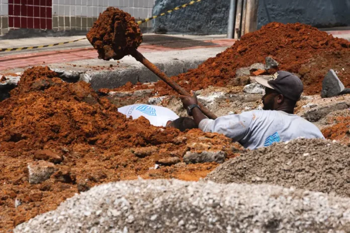 Trabalhador realiza escavação em via urbana para implantação do Plano Diretor de Drenagem Urbana em São José, ilustrando ações de infraestrutura para prevenção de alagamentos e melhoria do escoamento da água.
