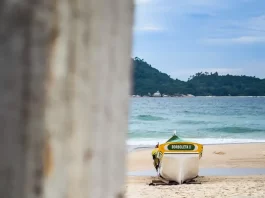 Barco de pesca artesanal na faixa de areia, com o mar ao fundo, em Florianópolis, ilustrando o cenário da safra da tainha e a importância da atividade pesqueira no litoral.