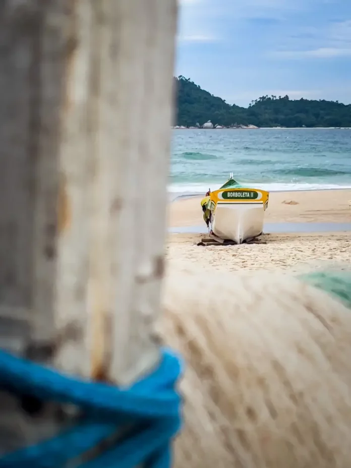 Barco de pesca artesanal na faixa de areia, com o mar ao fundo, em Florianópolis, ilustrando o cenário da safra da tainha e a importância da atividade pesqueira no litoral.