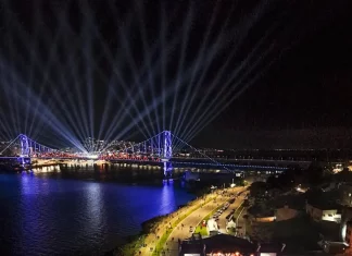 Centenário da Ponte Hercílio Luz reúne cerca de 100 mil pessoas no fim de semana Vista aérea mostra o público reunido na Beira-Mar Continental durante as comemorações do centenário da Ponte Hercílio Luz, em Florianópolis, com palco de shows, iluminação especial e feixes de luz sobre a ponte durante evento noturno.