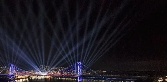 Centenário da Ponte Hercílio Luz reúne cerca de 100 mil pessoas no fim de semana Vista aérea mostra o público reunido na Beira-Mar Continental durante as comemorações do centenário da Ponte Hercílio Luz, em Florianópolis, com palco de shows, iluminação especial e feixes de luz sobre a ponte durante evento noturno.