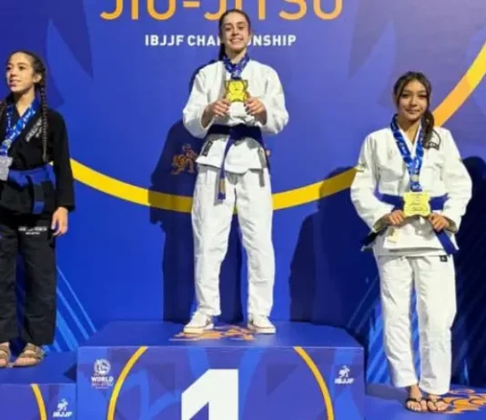 Atletas de jiu-jitsu posam no pódio durante o Campeonato Mundial da IBJJF, na Califórnia. Ao centro, Ester Boing aparece no lugar mais alto do pódio com a medalha de ouro, representando a conquista do título mundial da categoria faixa-azul. A imagem destaca o resultado histórico da atleta de São José no cenário internacional da modalidade.