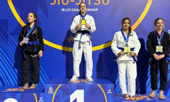 Ester Boing Atletas de jiu-jitsu posam no pódio durante o Campeonato Mundial da IBJJF, na Califórnia. Ao centro, Ester Boing aparece no lugar mais alto do pódio com a medalha de ouro, representando a conquista do título mundial da categoria faixa-azul. A imagem destaca o resultado histórico da atleta de São José no cenário internacional da modalidade.