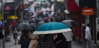 Pessoas caminhando com guarda-chuvas no centro da cidade, mostrando que a chuva voltou no final de semana