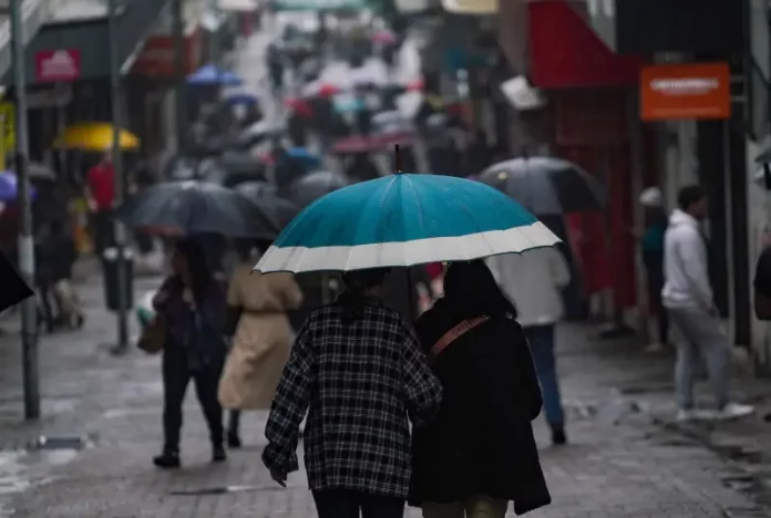 Pessoas caminhando com guarda-chuvas no centro da cidade, mostrando que a chuva voltou no final de semana