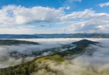 Frio intenso marca início da semana em Santa Catarina Vista aérea de uma região montanhosa de Santa Catarina coberta por nevoeiro e nuvens baixas ao amanhecer. A imagem mostra vegetação verde, morros e o céu parcialmente nublado, ilustrando o frio intenso e as condições típicas da massa de ar polar que atua no estado.