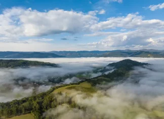 Frio intenso marca início da semana em Santa Catarina Vista aérea de uma região montanhosa de Santa Catarina coberta por nevoeiro e nuvens baixas ao amanhecer. A imagem mostra vegetação verde, morros e o céu parcialmente nublado, ilustrando o frio intenso e as condições típicas da massa de ar polar que atua no estado.