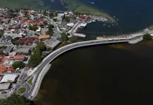 Imagem aérea da nova ponte da Lagoa da Conceição, em Florianópolis, mostrando a estrutura sobre a água, o tráfego de veículos e a ligação viária entre as margens, destacando sua função de melhorar a mobilidade e o acesso às praias do Leste.