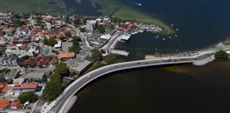 Imagem aérea da nova ponte da Lagoa da Conceição, em Florianópolis, mostrando a estrutura sobre a água, o tráfego de veículos e a ligação viária entre as margens, destacando sua função de melhorar a mobilidade e o acesso às praias do Leste.