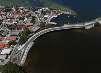 Imagem aérea da nova ponte da Lagoa da Conceição, em Florianópolis, mostrando a estrutura sobre a água, o tráfego de veículos e a ligação viária entre as margens, destacando sua função de melhorar a mobilidade e o acesso às praias do Leste.