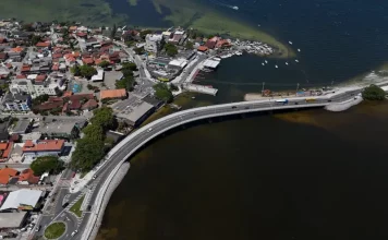 Imagem aérea da nova ponte da Lagoa da Conceição, em Florianópolis, mostrando a estrutura sobre a água, o tráfego de veículos e a ligação viária entre as margens, destacando sua função de melhorar a mobilidade e o acesso às praias do Leste.
