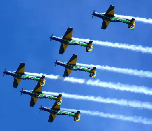 Esquadrilha da Fumaça se apresenta em Florianópolis neste domingo Seis aeronaves da Esquadrilha da Fumaça realizam voo em formação no céu azul, deixando rastros de fumaça branca. A imagem ilustra a apresentação aérea anunciada para Florianópolis e destaca o caráter de espetáculo visual e demonstração de precisão da Força Aérea Brasileira para o público.