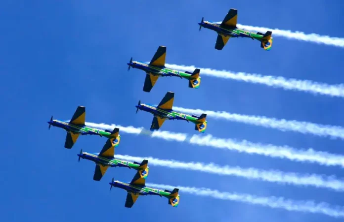 Esquadrilha da Fumaça Seis aeronaves da Esquadrilha da Fumaça realizam voo em formação no céu azul, deixando rastros de fumaça branca. A imagem ilustra a apresentação aérea anunciada para Florianópolis e destaca o caráter de espetáculo visual e demonstração de precisão da Força Aérea Brasileira para o público.