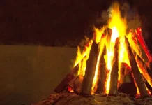 Fogueira acesa com toras de madeira empilhadas em formato triangular durante a noite. A imagem ilustra o tema das ocorrências com fogueiras e os cuidados necessários para prevenir queimaduras e incêndios durante as festas juninas.