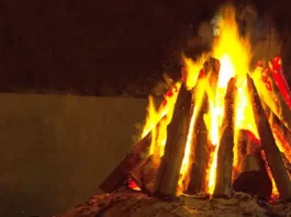 Fogueira acesa com toras de madeira empilhadas em formato triangular durante a noite. A imagem ilustra o tema das ocorrências com fogueiras e os cuidados necessários para prevenir queimaduras e incêndios durante as festas juninas.