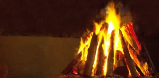 Fogueira acesa com toras de madeira empilhadas em formato triangular durante a noite. A imagem ilustra o tema das ocorrências com fogueiras e os cuidados necessários para prevenir queimaduras e incêndios durante as festas juninas.