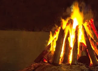 Fogueira acesa com toras de madeira empilhadas em formato triangular durante a noite. A imagem ilustra o tema das ocorrências com fogueiras e os cuidados necessários para prevenir queimaduras e incêndios durante as festas juninas.