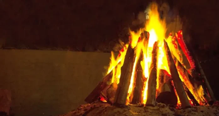 Fogueira acesa com toras de madeira empilhadas em formato triangular durante a noite. A imagem ilustra o tema das ocorrências com fogueiras e os cuidados necessários para prevenir queimaduras e incêndios durante as festas juninas.