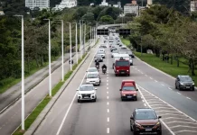 Vista de uma avenida movimentada em Florianópolis, com carros circulando em múltiplas faixas e área urbana ao fundo. A imagem ilustra a expansão da mobilidade urbana e a implantação de pontos de recarga para veículos elétricos em espaços públicos da cidade.