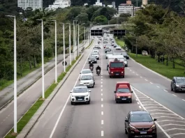 Florianópolis aprova 34 pontos de recarga para veículos elétricos em espaços públicos. Vista de uma avenida movimentada em Florianópolis, com carros circulando em múltiplas faixas e área urbana ao fundo. A imagem ilustra a expansão da mobilidade urbana e a implantação de pontos de recarga para veículos elétricos em espaços públicos da cidade.