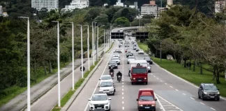 Vista de uma avenida movimentada em Florianópolis, com carros circulando em múltiplas faixas e área urbana ao fundo. A imagem ilustra a expansão da mobilidade urbana e a implantação de pontos de recarga para veículos elétricos em espaços públicos da cidade.