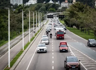 Florianópolis aprova 34 pontos de recarga para veículos elétricos em espaços públicos. Vista de uma avenida movimentada em Florianópolis, com carros circulando em múltiplas faixas e área urbana ao fundo. A imagem ilustra a expansão da mobilidade urbana e a implantação de pontos de recarga para veículos elétricos em espaços públicos da cidade.