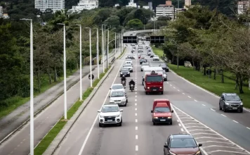 Florianópolis aprova 34 pontos de recarga para veículos elétricos em espaços públicos. Vista de uma avenida movimentada em Florianópolis, com carros circulando em múltiplas faixas e área urbana ao fundo. A imagem ilustra a expansão da mobilidade urbana e a implantação de pontos de recarga para veículos elétricos em espaços públicos da cidade.