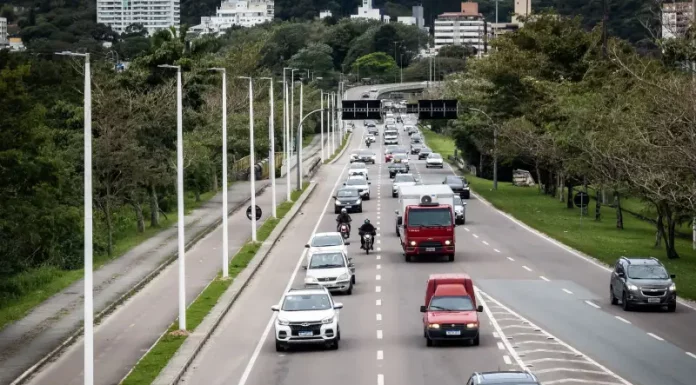 Florianópolis aprova 34 pontos de recarga para veículos elétricos em espaços públicos. Vista de uma avenida movimentada em Florianópolis, com carros circulando em múltiplas faixas e área urbana ao fundo. A imagem ilustra a expansão da mobilidade urbana e a implantação de pontos de recarga para veículos elétricos em espaços públicos da cidade.