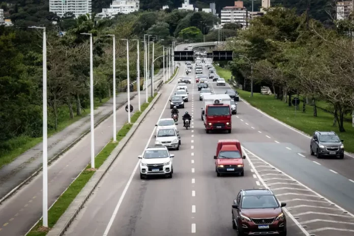 Vista de uma avenida movimentada em Florianópolis, com carros circulando em múltiplas faixas e área urbana ao fundo. A imagem ilustra a expansão da mobilidade urbana e a implantação de pontos de recarga para veículos elétricos em espaços públicos da cidade.