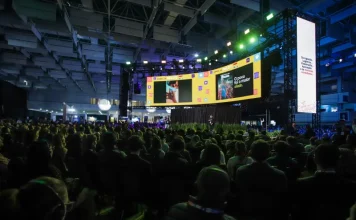 Auditório lotado durante uma edição do Summit Cidades, com público sentado diante de um grande palco iluminado e telões exibindo apresentações. A imagem ilustra a dimensão do evento, que reúne milhares de participantes para debater gestão pública, desenvolvimento urbano, inovação, mobilidade e políticas para o futuro das cidades em Florianópolis.