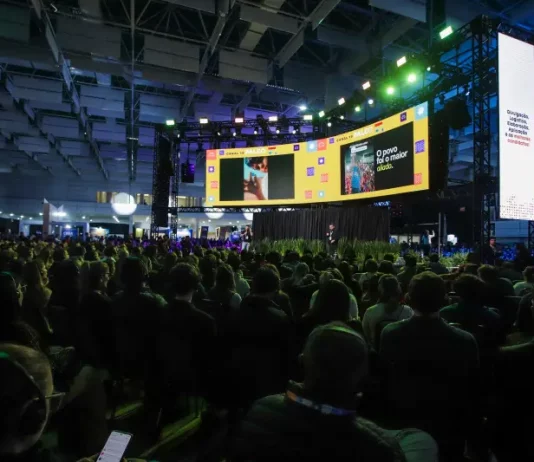 Auditório lotado durante uma edição do Summit Cidades, com público sentado diante de um grande palco iluminado e telões exibindo apresentações. A imagem ilustra a dimensão do evento, que reúne milhares de participantes para debater gestão pública, desenvolvimento urbano, inovação, mobilidade e políticas para o futuro das cidades em Florianópolis.