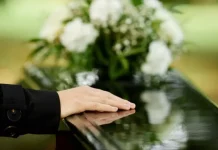 a foto apresenta a mão de uma pessoa sobre um caixão, em um velório, representando a Central Funerária de São José