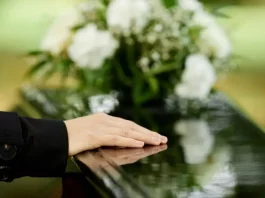 a foto apresenta a mão de uma pessoa sobre um caixão, em um velório, representando a Central Funerária de São José