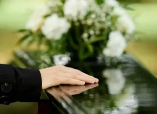 a foto apresenta a mão de uma pessoa sobre um caixão, em um velório, representando a Central Funerária de São José