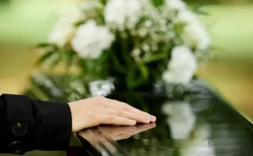 a foto apresenta a mão de uma pessoa sobre um caixão, em um velório, representando a Central Funerária de São José
