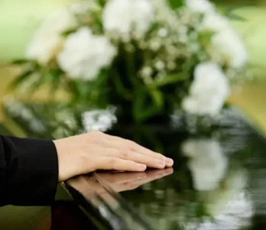 a foto apresenta a mão de uma pessoa sobre um caixão, em um velório, representando a Central Funerária de São José