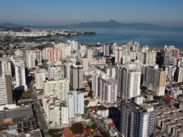 São José regulamenta outorga onerosa e define regras para construção e mudança de uso de imóveis Vista aérea da região central e da área litorânea de São José, com prédios residenciais e comerciais próximos à Baía Sul. A imagem ilustra o crescimento urbano do município e a regulamentação da outorga onerosa, mecanismo que permite ampliar o potencial construtivo e alterar o uso de imóveis mediante contrapartida financeira.