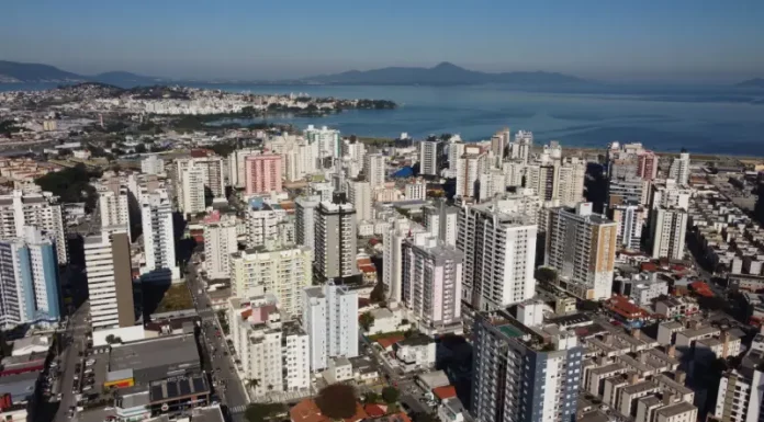 São José regulamenta outorga onerosa e define regras para construção e mudança de uso de imóveis Vista aérea da região central e da área litorânea de São José, com prédios residenciais e comerciais próximos à Baía Sul. A imagem ilustra o crescimento urbano do município e a regulamentação da outorga onerosa, mecanismo que permite ampliar o potencial construtivo e alterar o uso de imóveis mediante contrapartida financeira.