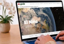 Pessoa utiliza um notebook exibindo a página especial “Fenômeno Climático El Niño” no portal da Secretaria de Estado da Proteção e Defesa Civil de Santa Catarina (SDC/SC). A imagem ilustra o acesso à plataforma criada para divulgar informações atualizadas, orientações de prevenção, documentos oficiais e conteúdos educativos sobre os impactos do El Niño e as ações de preparação da Defesa Civil no estado.