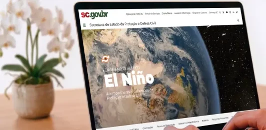 Pessoa utiliza um notebook exibindo a página especial “Fenômeno Climático El Niño” no portal da Secretaria de Estado da Proteção e Defesa Civil de Santa Catarina (SDC/SC). A imagem ilustra o acesso à plataforma criada para divulgar informações atualizadas, orientações de prevenção, documentos oficiais e conteúdos educativos sobre os impactos do El Niño e as ações de preparação da Defesa Civil no estado.
