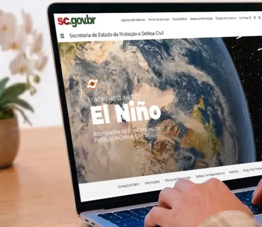 Defesa Civil de SC lança página com informações e orientações sobre El Niño Pessoa utiliza um notebook exibindo a página especial “Fenômeno Climático El Niño” no portal da Secretaria de Estado da Proteção e Defesa Civil de Santa Catarina (SDC/SC). A imagem ilustra o acesso à plataforma criada para divulgar informações atualizadas, orientações de prevenção, documentos oficiais e conteúdos educativos sobre os impactos do El Niño e as ações de preparação da Defesa Civil no estado.