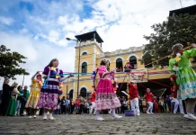 Dia do Manezinho celebra cultura e tradições de Florianópolis Participantes vestidos com trajes coloridos realizam uma apresentação cultural em frente ao Mercado Público de Florianópolis durante uma celebração do Dia do Manezinho. A imagem ilustra a valorização das tradições, da cultura popular e das manifestações folclóricas que fazem parte da identidade da cidade.