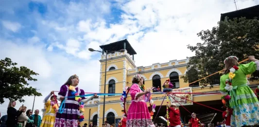 Dia do Manezinho celebra cultura e tradições de Florianópolis Participantes vestidos com trajes coloridos realizam uma apresentação cultural em frente ao Mercado Público de Florianópolis durante uma celebração do Dia do Manezinho. A imagem ilustra a valorização das tradições, da cultura popular e das manifestações folclóricas que fazem parte da identidade da cidade.