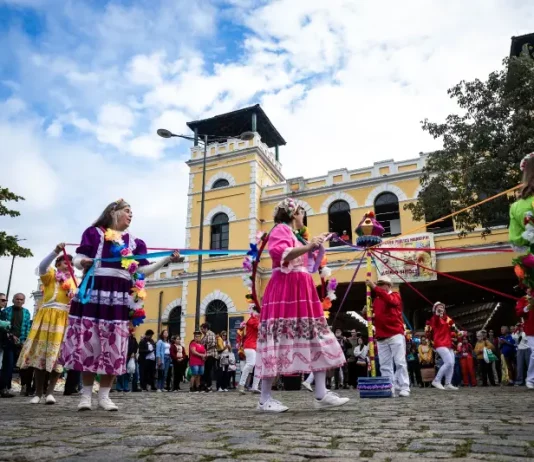 Dia do Manezinho celebra cultura e tradições de Florianópolis Participantes vestidos com trajes coloridos realizam uma apresentação cultural em frente ao Mercado Público de Florianópolis durante uma celebração do Dia do Manezinho. A imagem ilustra a valorização das tradições, da cultura popular e das manifestações folclóricas que fazem parte da identidade da cidade.