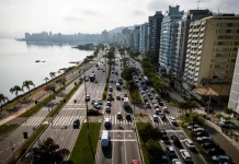 Florianópolis envia à Câmara projeto de nova regulamentação do transporte por aplicativo Vista aérea de uma avenida à beira-mar em Florianópolis com intenso fluxo de veículos e prédios residenciais ao lado. A imagem ilustra o contexto da mobilidade urbana na Capital e acompanha matéria sobre projeto de lei que atualiza as regras do transporte por aplicativos para ampliar segurança, fiscalização e qualidade do serviço.