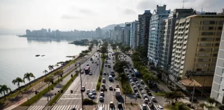 Vista aérea de uma avenida à beira-mar em Florianópolis com intenso fluxo de veículos e prédios residenciais ao lado. A imagem ilustra o contexto da mobilidade urbana na Capital e acompanha matéria sobre projeto de lei que atualiza as regras do transporte por aplicativos para ampliar segurança, fiscalização e qualidade do serviço.